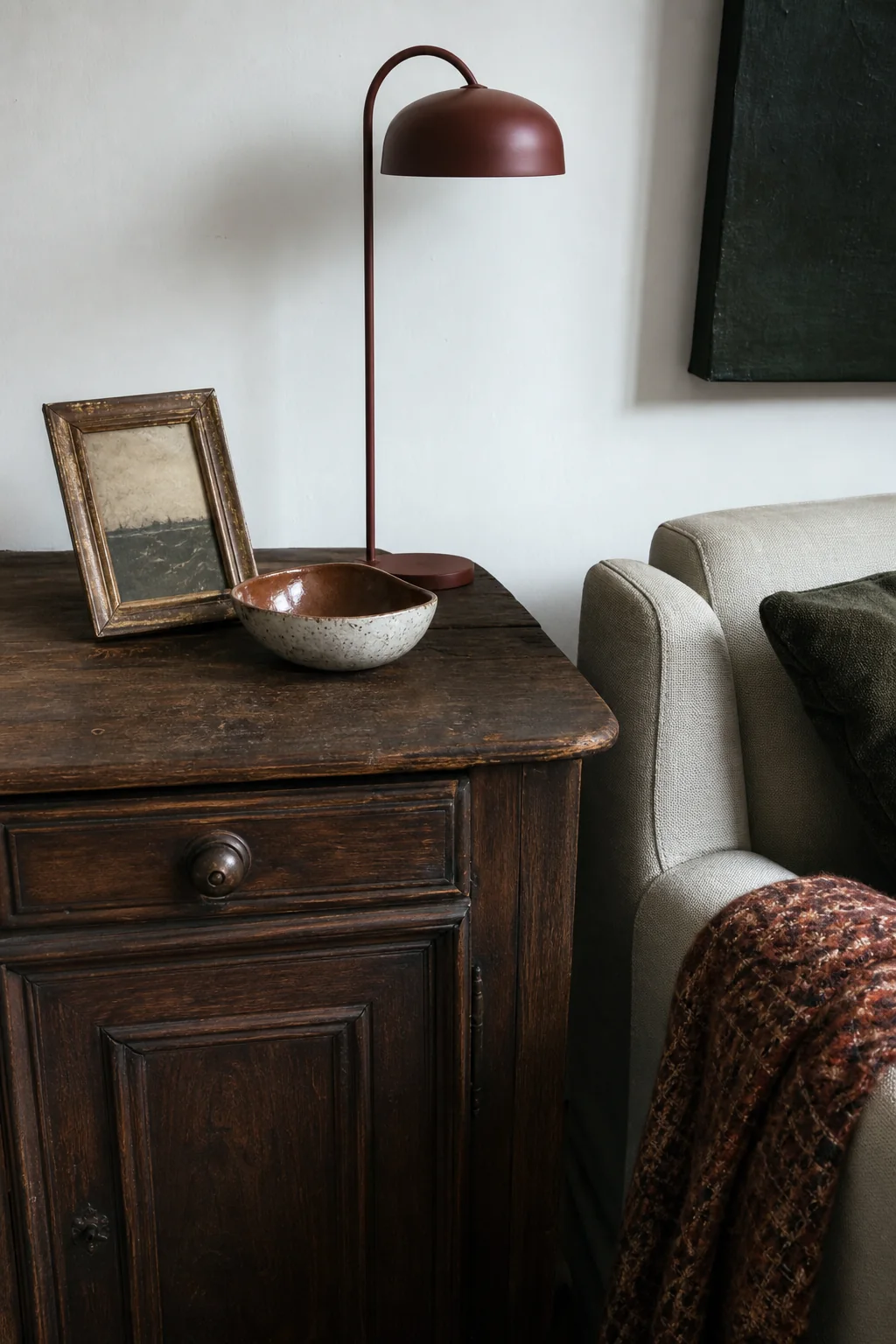 Aged dark timber cabinet beside a clean-lined sofa, modern rust lamp, handmade bowl and patterned wool textile