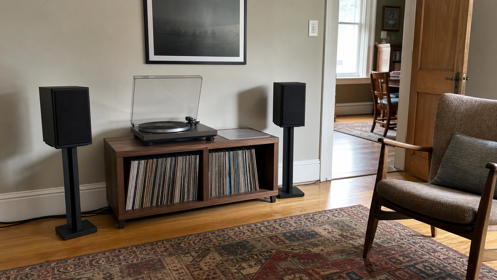 Modest living-room record corner with a turntable on a stable cabinet, upright albums, separate speakers and a usable chair.