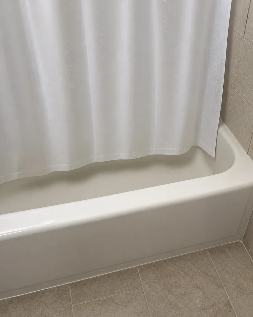 Close view of an inner shower curtain hem hanging inside a tub with clearance from the tub floor and coverage at the end.